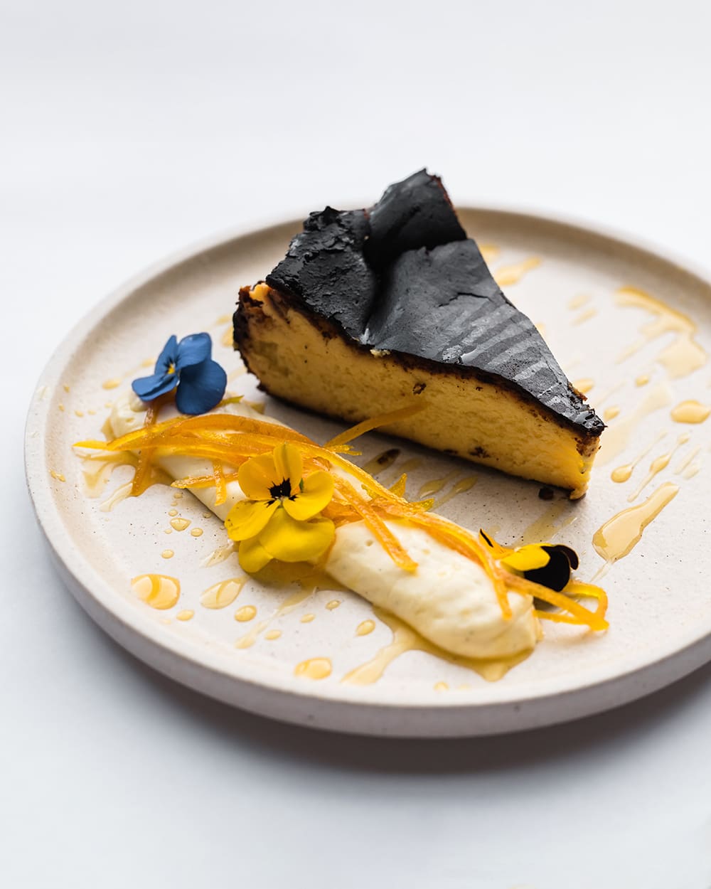 Basque cheesecake from The Commodore Mount Gambier dessert menu, on a cream plate and white table cloth with flower and yellow edible garnishes.